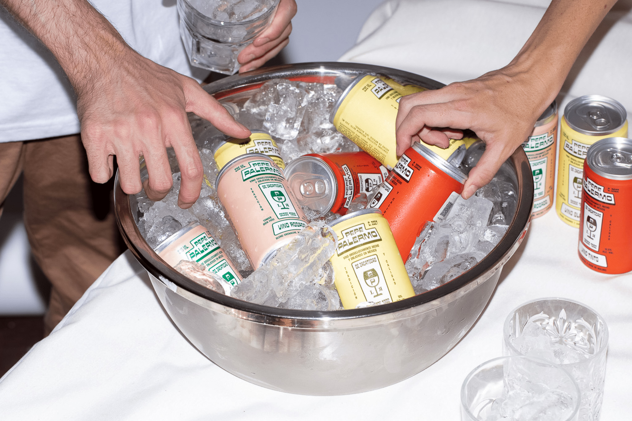 Hands reaching into a metal bowl filled with ice and Pepe Palermo canned wine.