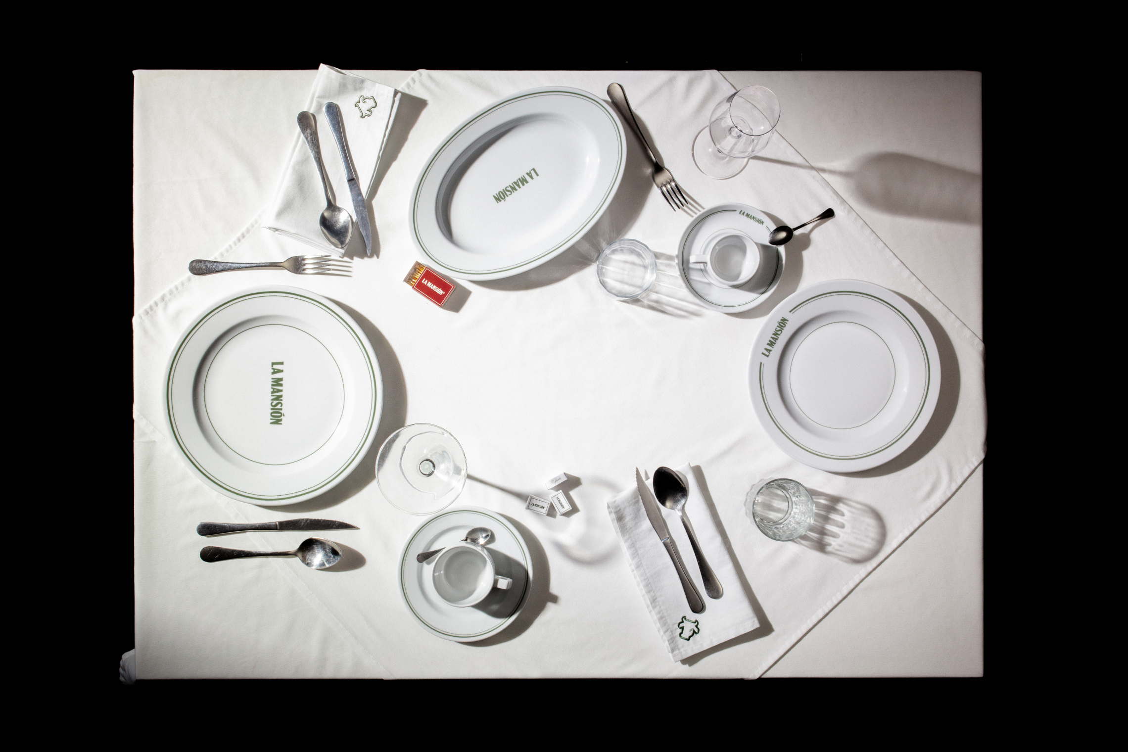 Mesa con loza personalizada de La Mansión sobre mantel blanco.
