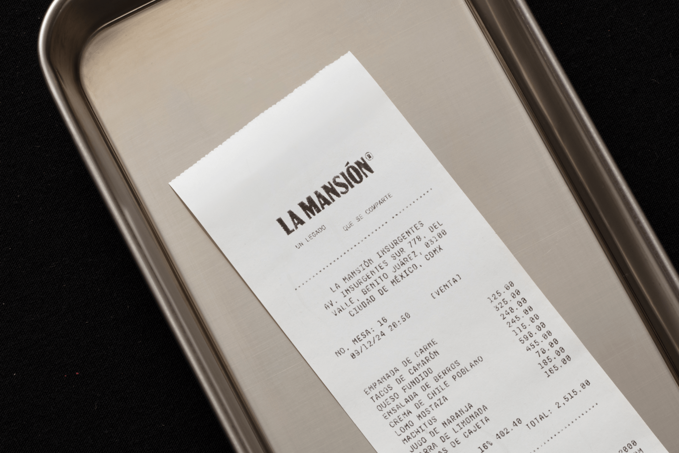 Receipt from La Mansión restaurant with brand identity printed and displayed on a metal tray.