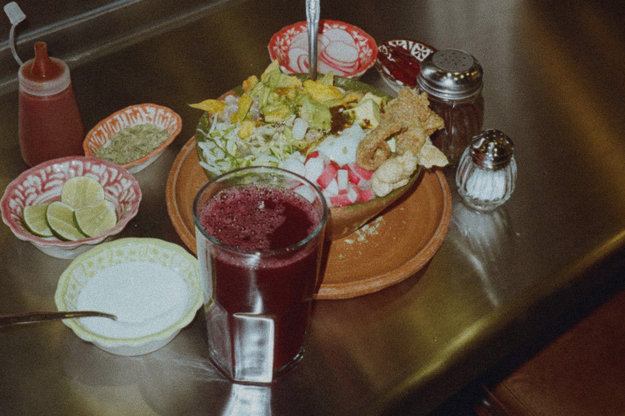 Analog photo of pozole dish with sides and drink, served on traditional Mexican tableware.